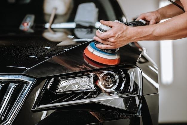 Detailer machine-polishing a glossy black car in a dark studio